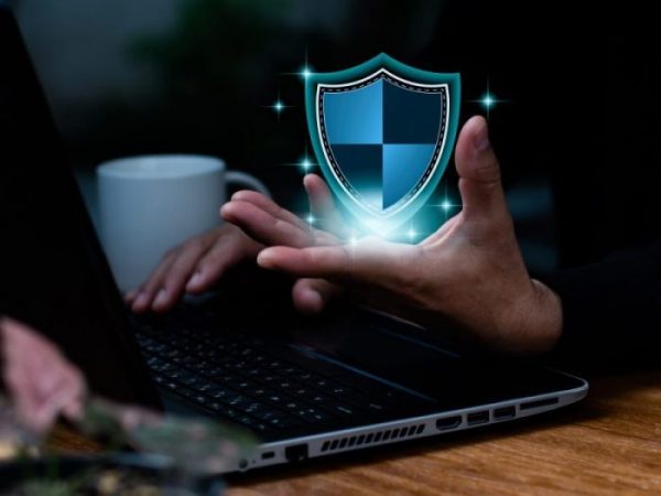 A business professional holding a digital security shield above a laptop, symbolizing cybersecurity protection, risk management, and insurance coverage gaps.